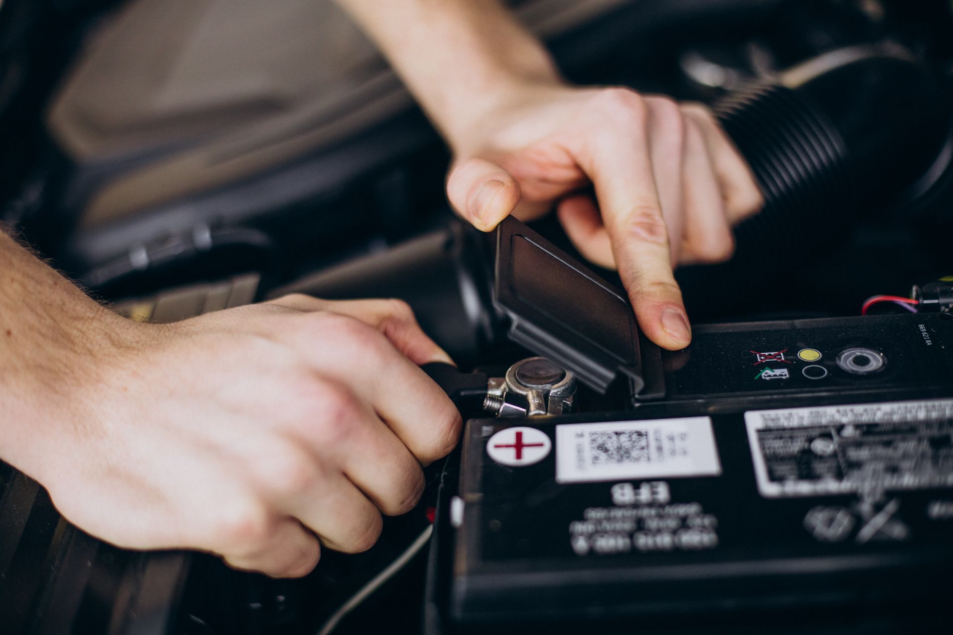 Hands connecting a battery terminal in a car engine compartment.