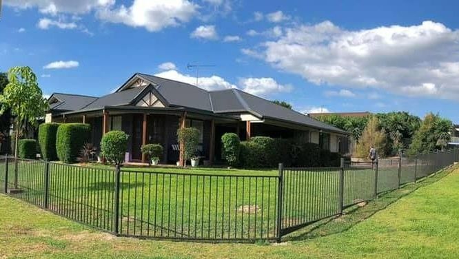 A Brown Fence With Yellow Pillars is Surrounded by Rocks and Grass — RBG Building & Maintenance in Cooloola Cove, QLD