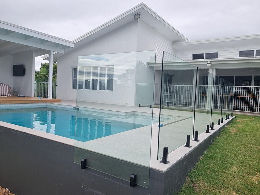 A Large Swimming Pool With a Glass Fence Around It — RBG Building & Maintenance in Veteran, QLD
