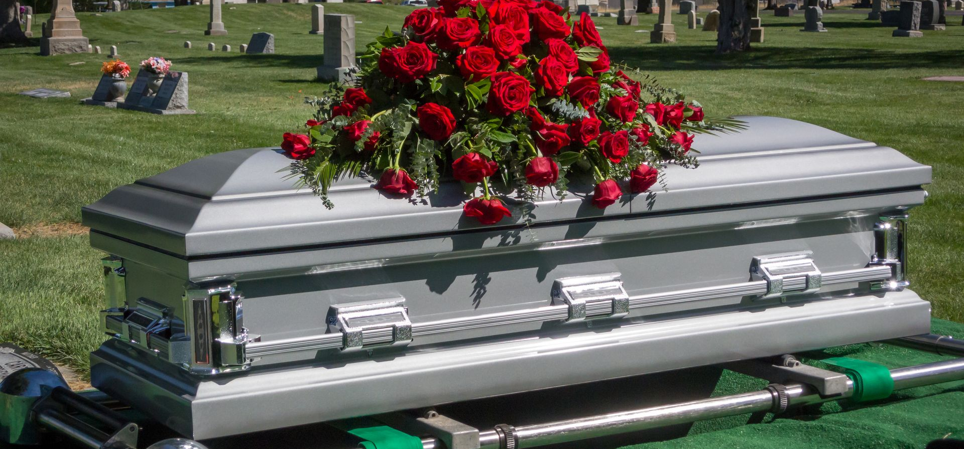 Silver casket adorned with red roses on a lawn cemetery