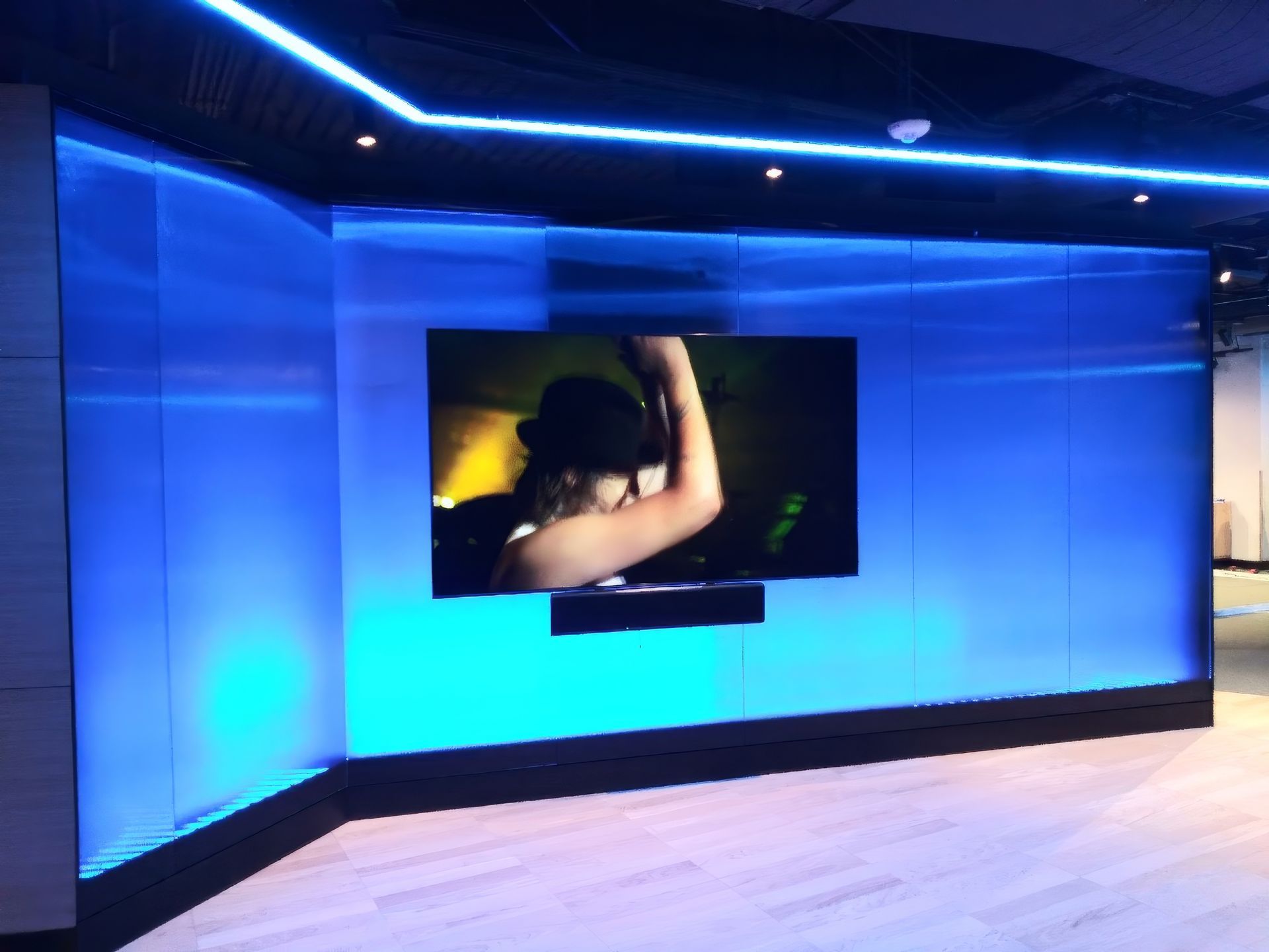 Blue-lit modern room with a wall-mounted screen showing a dancer and a large empty floor.