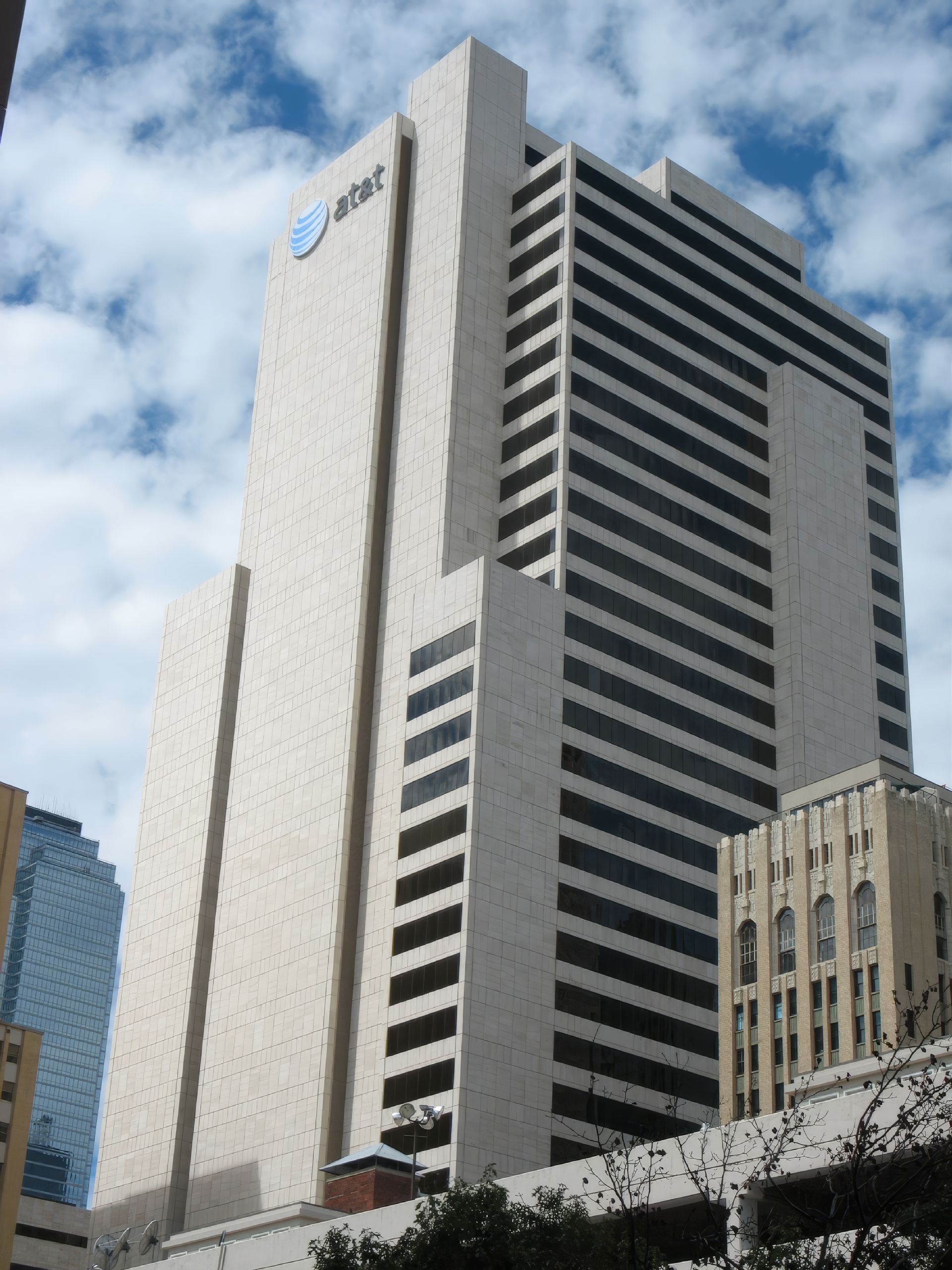 Tall modern office building with striped facade and a logo, seen against a cloudy sky.