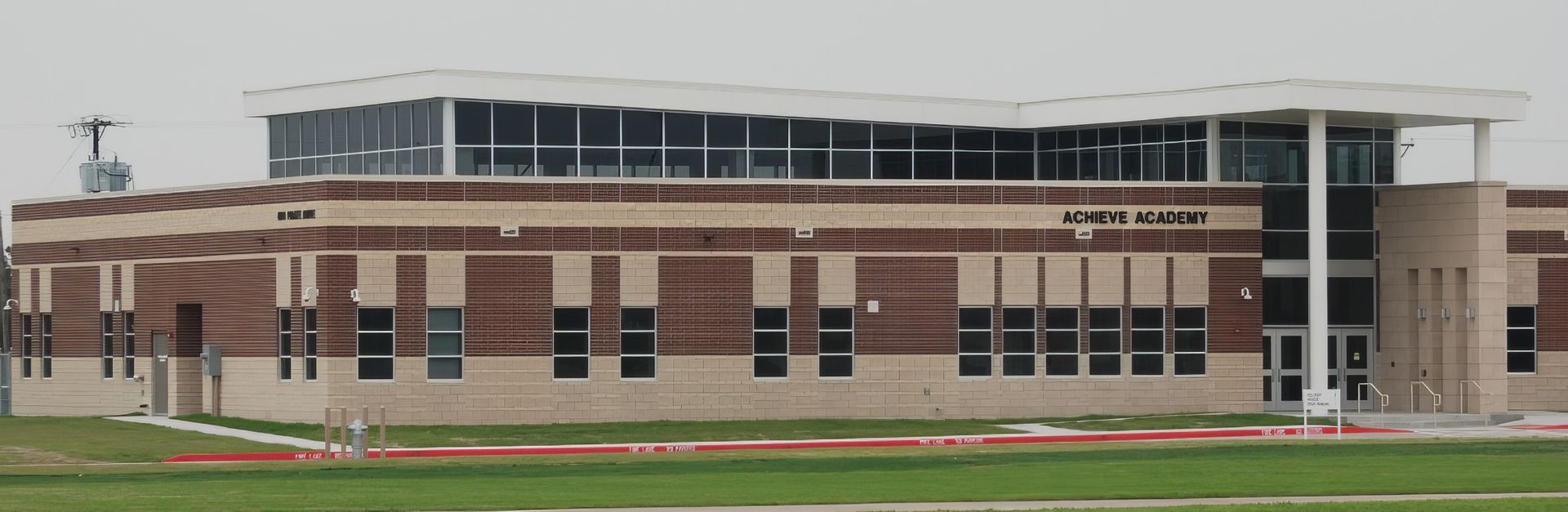Large modern brick school building with rows of windows and a glass entrance under a cloudy sky