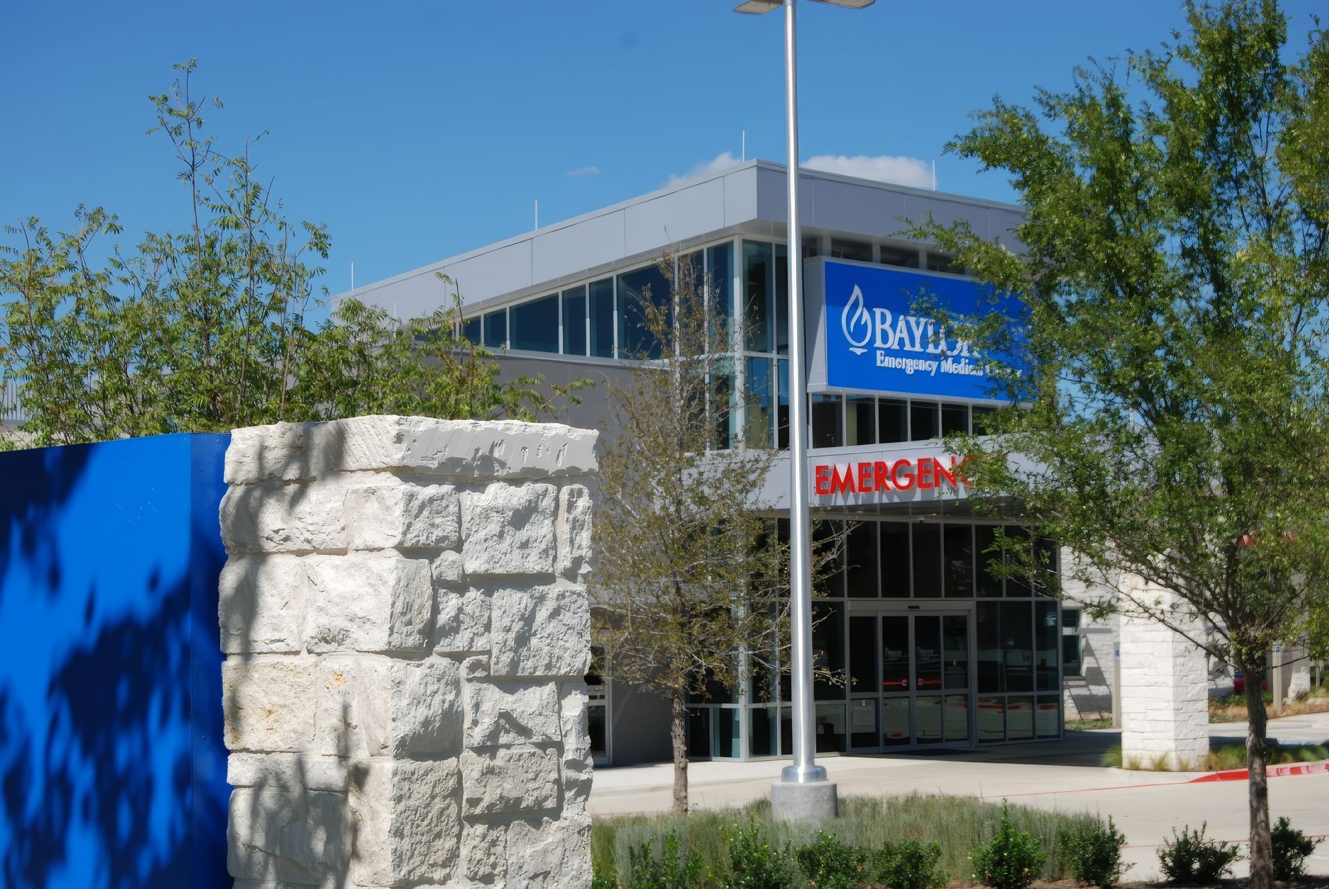 Modern building entrance with blue sign, stone wall, and trees in front
