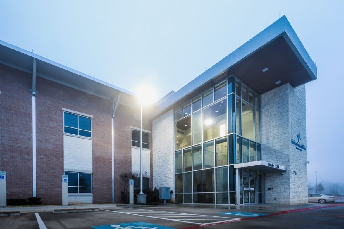 Modern brick-and-glass office building entrance at dawn with bright sun flare