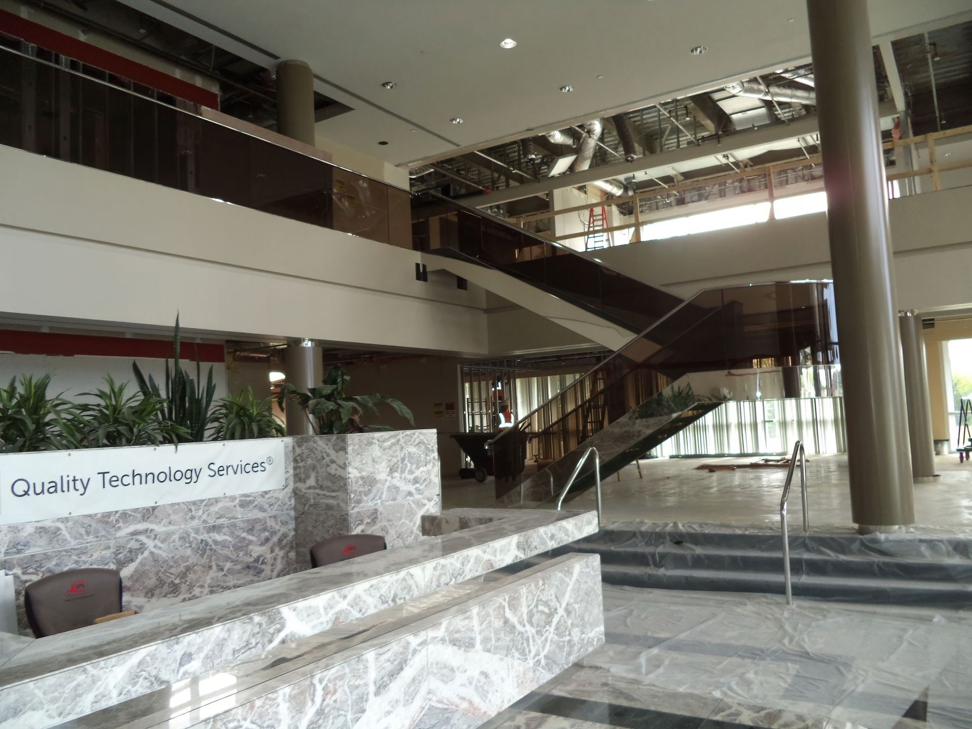 Modern lobby with marble reception desk, staircase, and glass railings under bright natural light