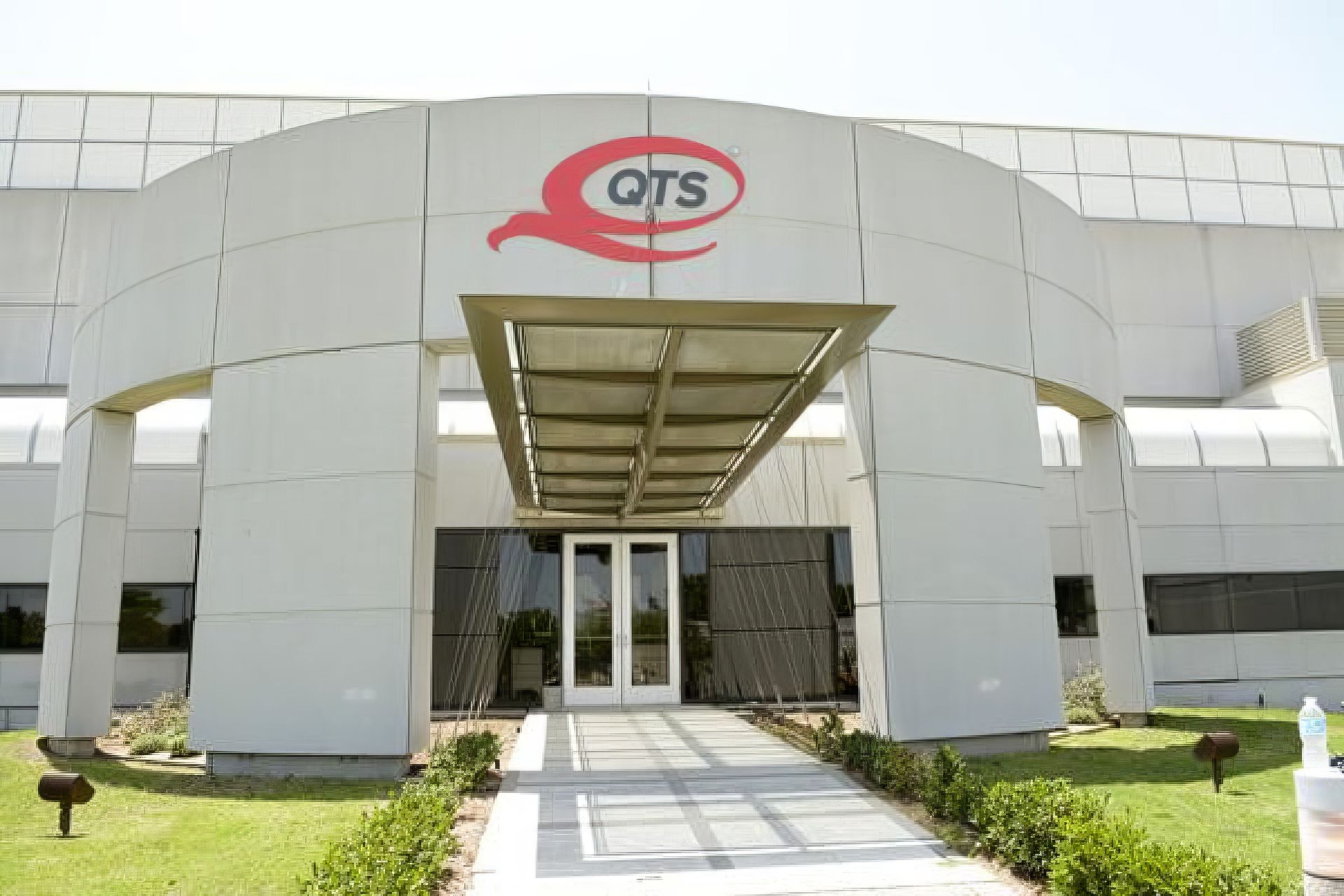 Modern white building entrance with a glass canopy and red GTS logo above the doors