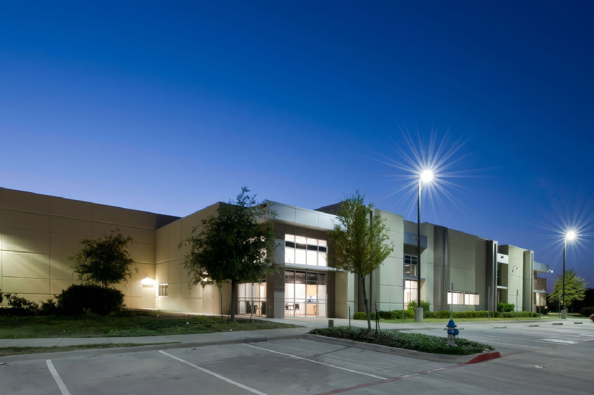Modern office building exterior at dusk with bright parking lot lights and a clear blue sky