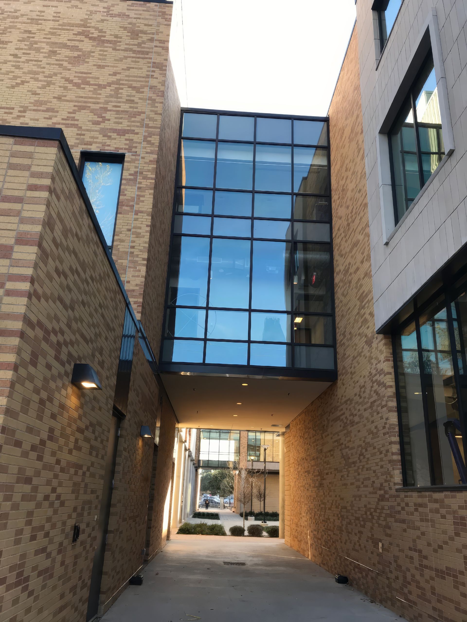 Modern brick-and-glass corridor between buildings with a skybridge and blue reflections