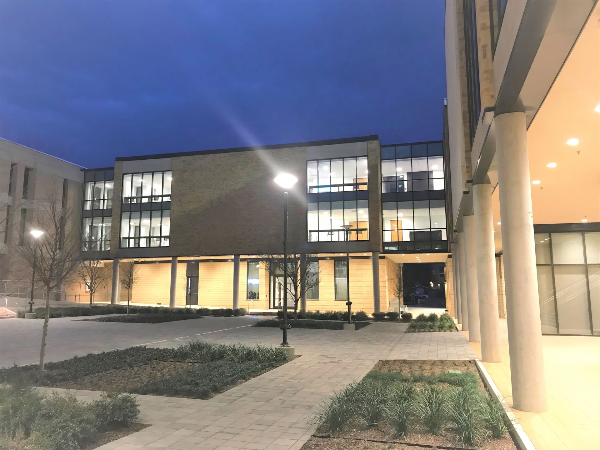 Modern building courtyard at dusk with lit windows, walkway, and snow-covered ground