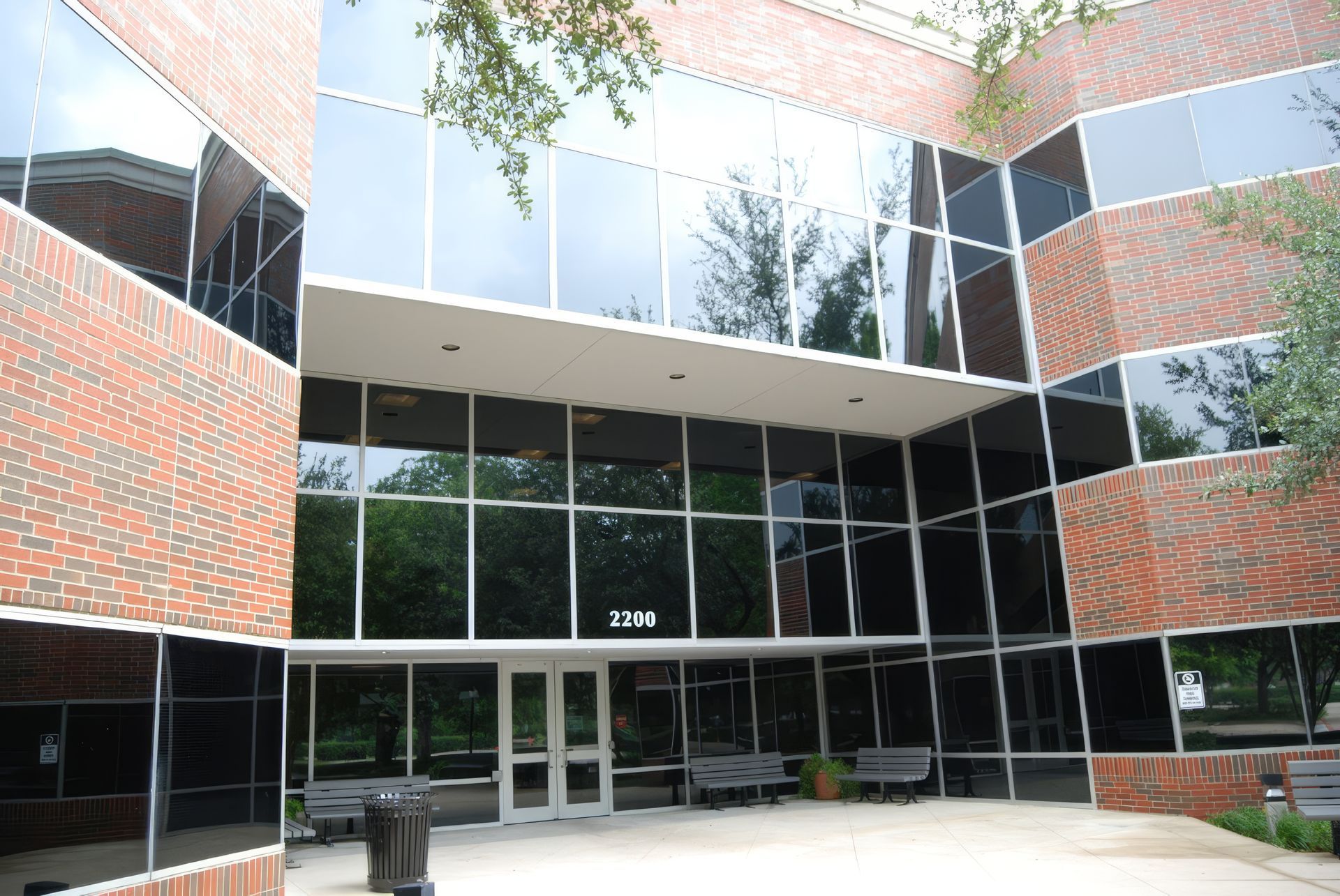 Modern brick-and-glass office building entrance with reflective windows and courtyard seating