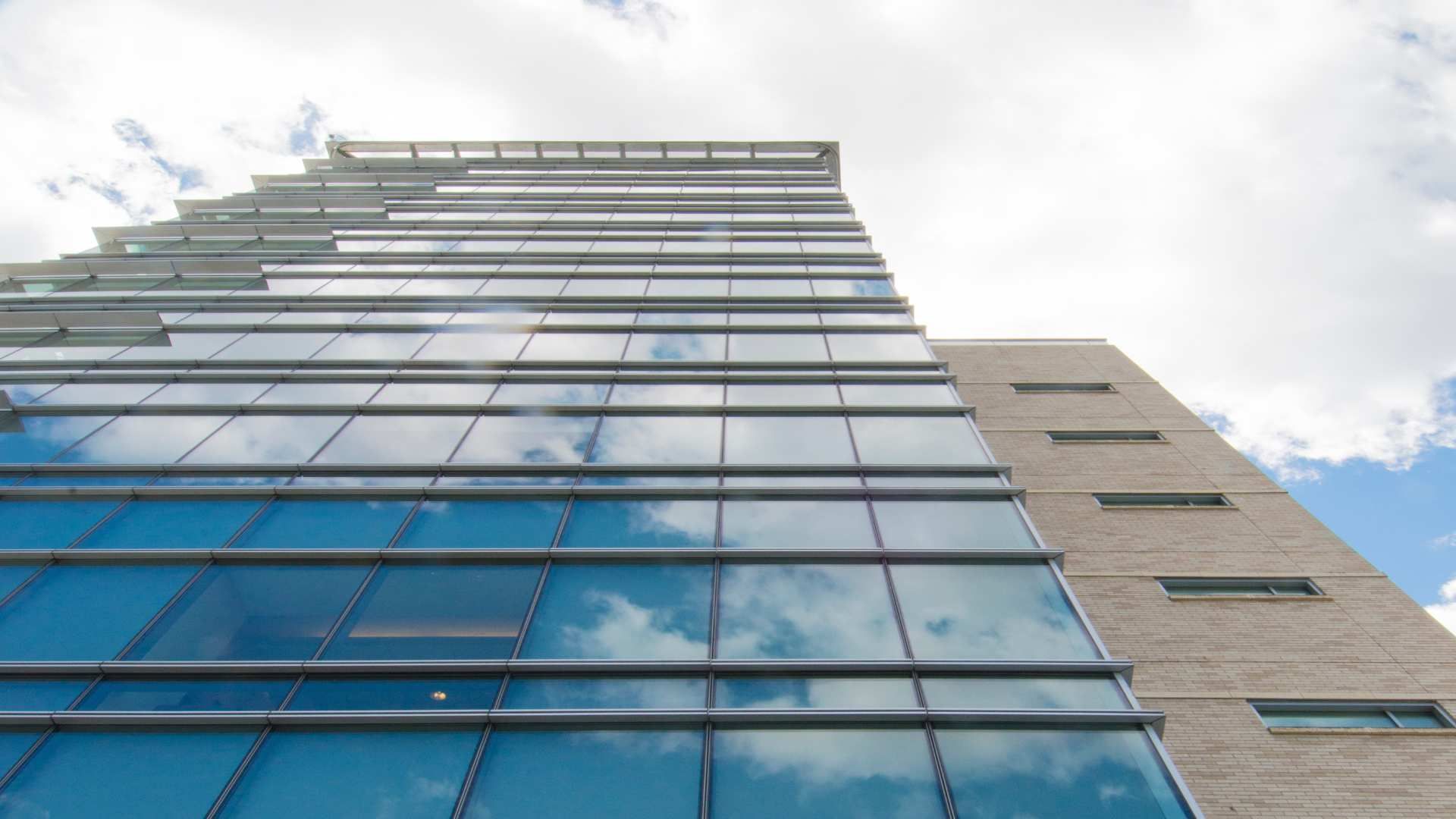 Low-angle view of a modern glass-and-brick office building against a cloudy sky