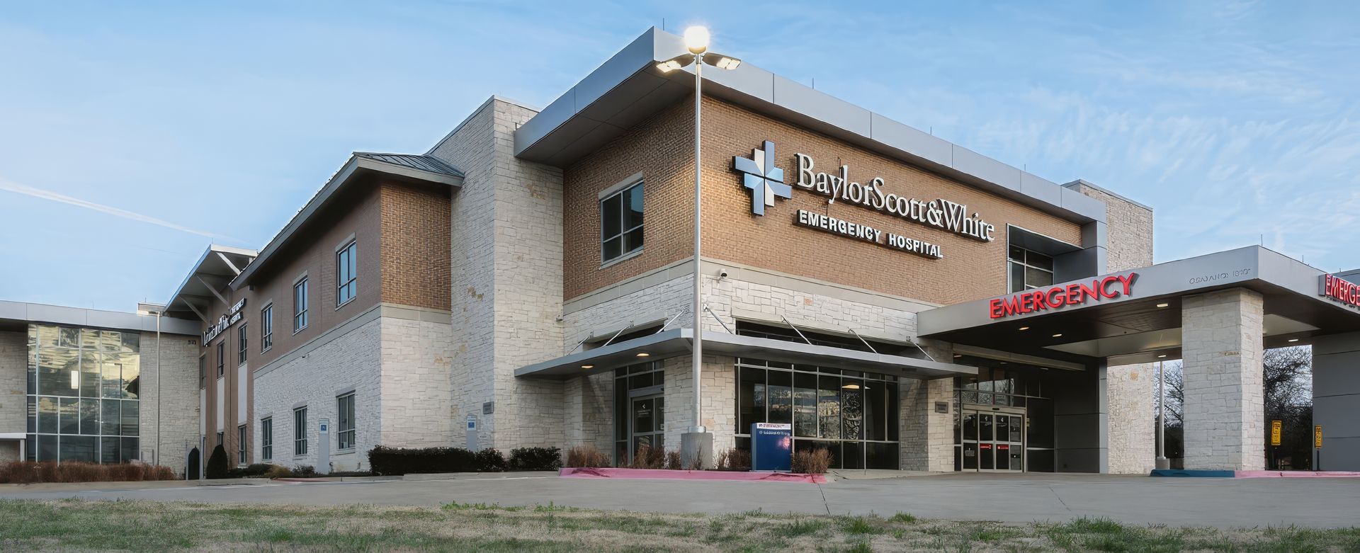 Modern hospital building exterior with tan brick, glass entrance, and covered drop-off area