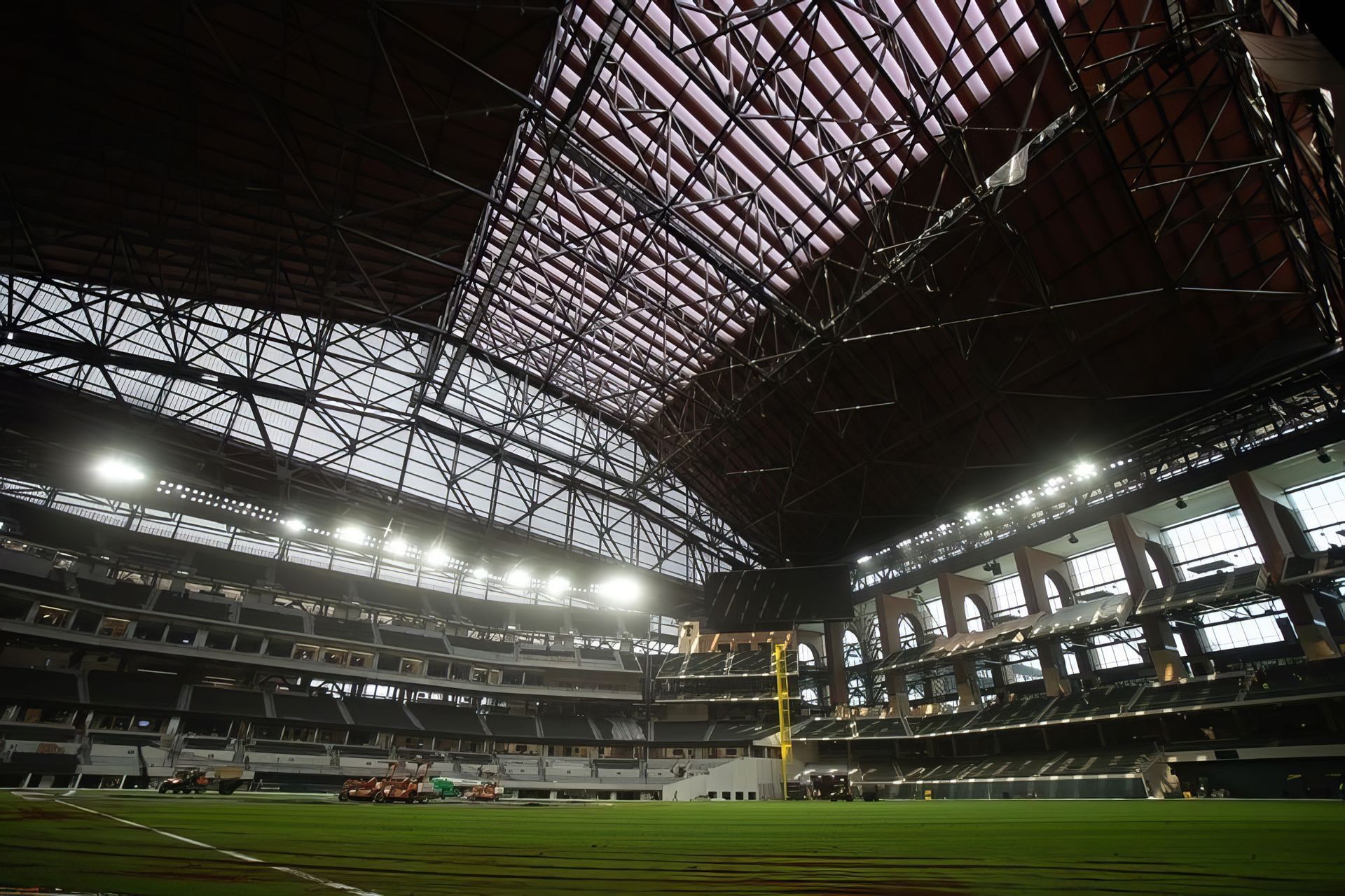 Wide-angle view of a mostly empty indoor stadium with a green field and arched roof structure