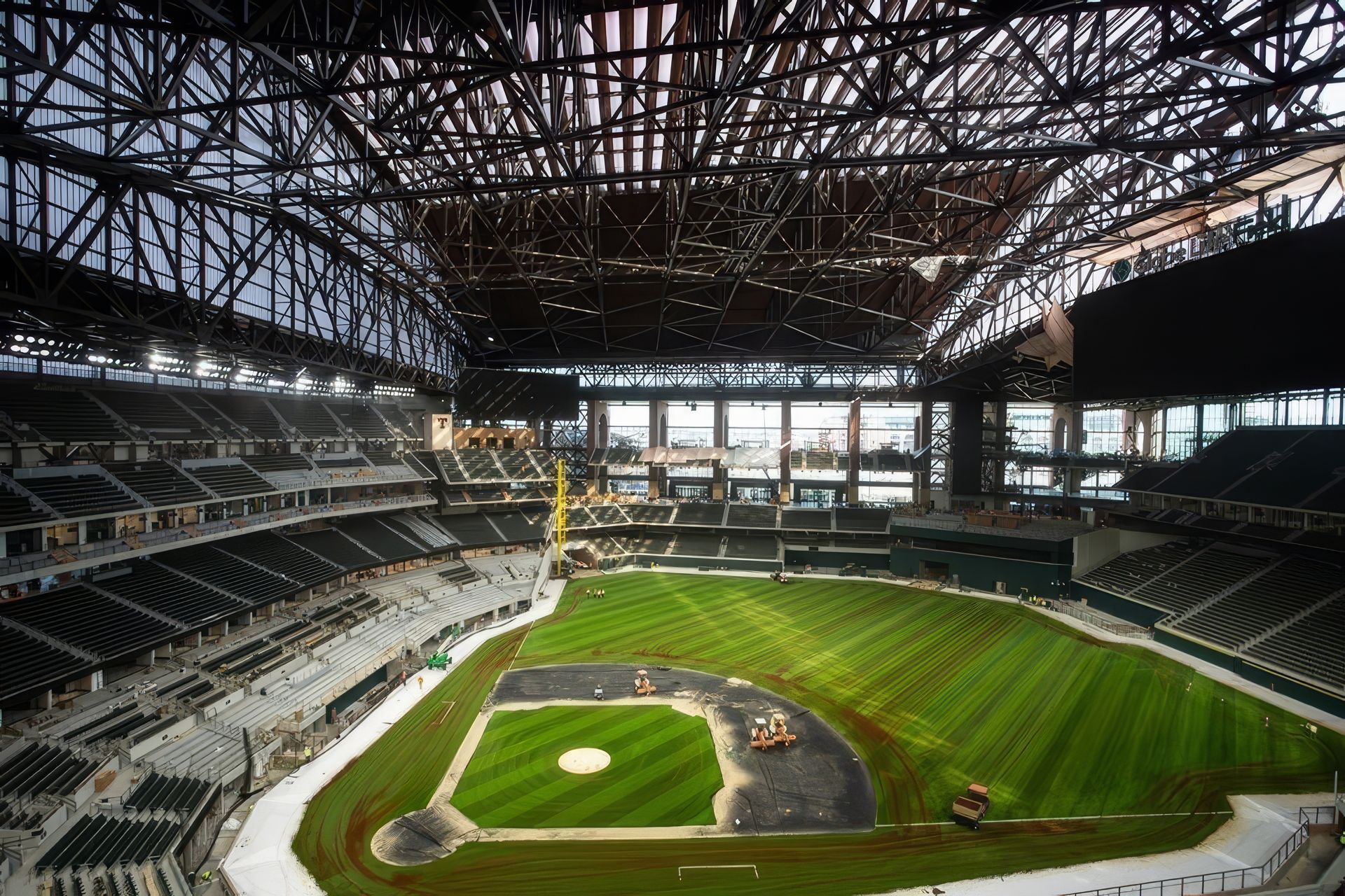 Empty baseball stadium with a dirt infield and green field under an open steel roof