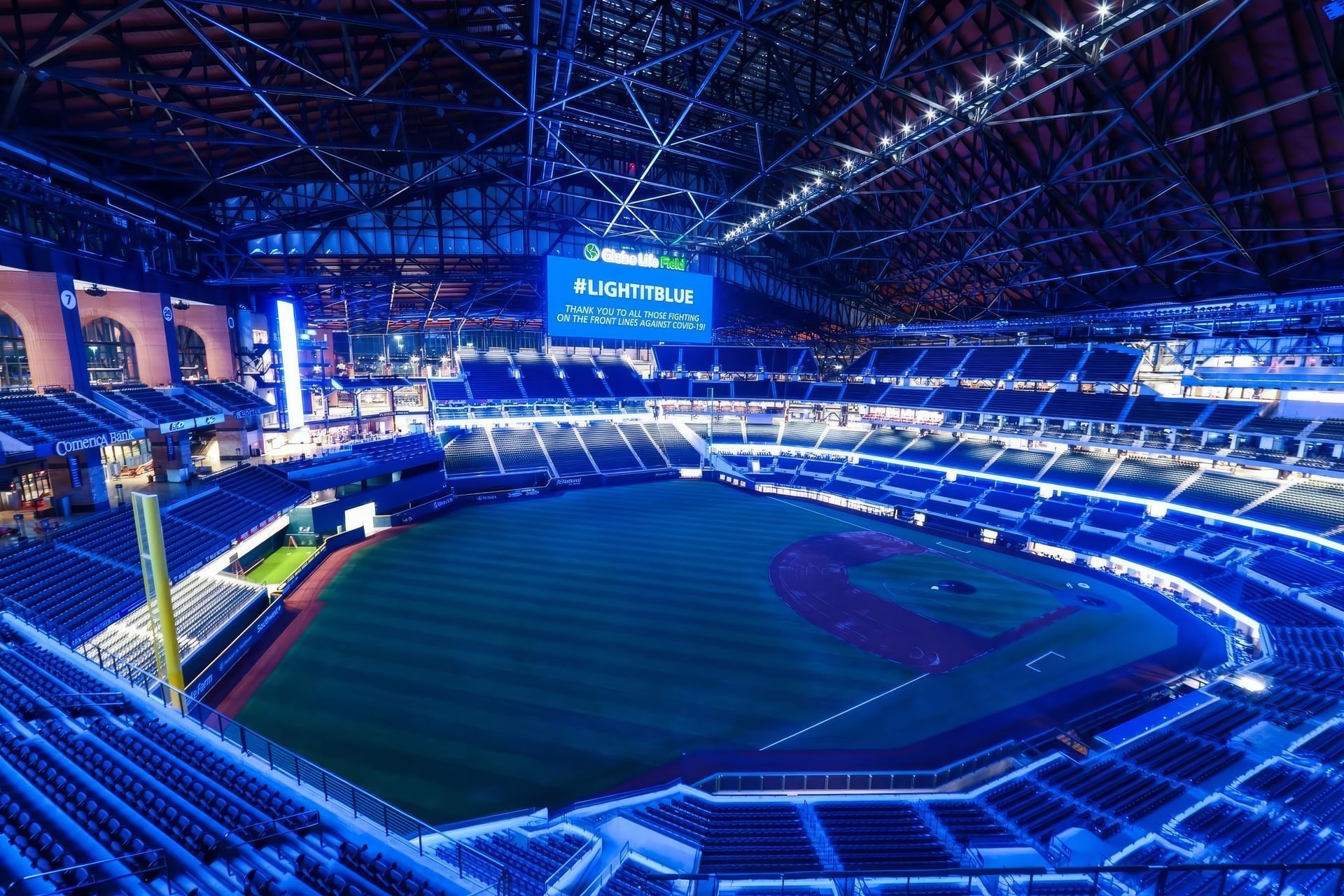 Empty baseball stadium lit in blue at night, viewed from the stands with the field and scoreboard visible