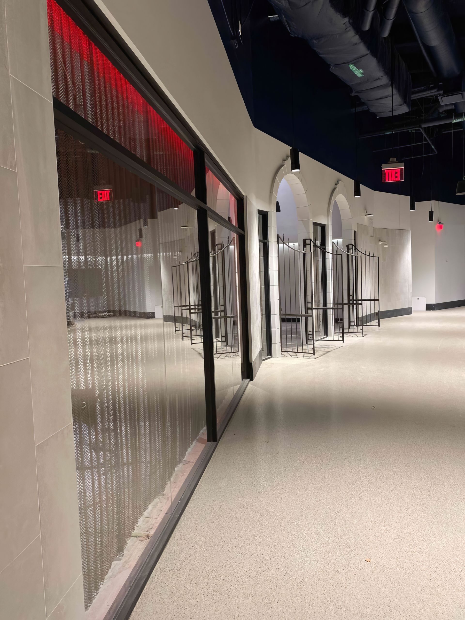 Quiet hallway with frosted glass walls, red accent lighting, and stacked chairs along the right side.
