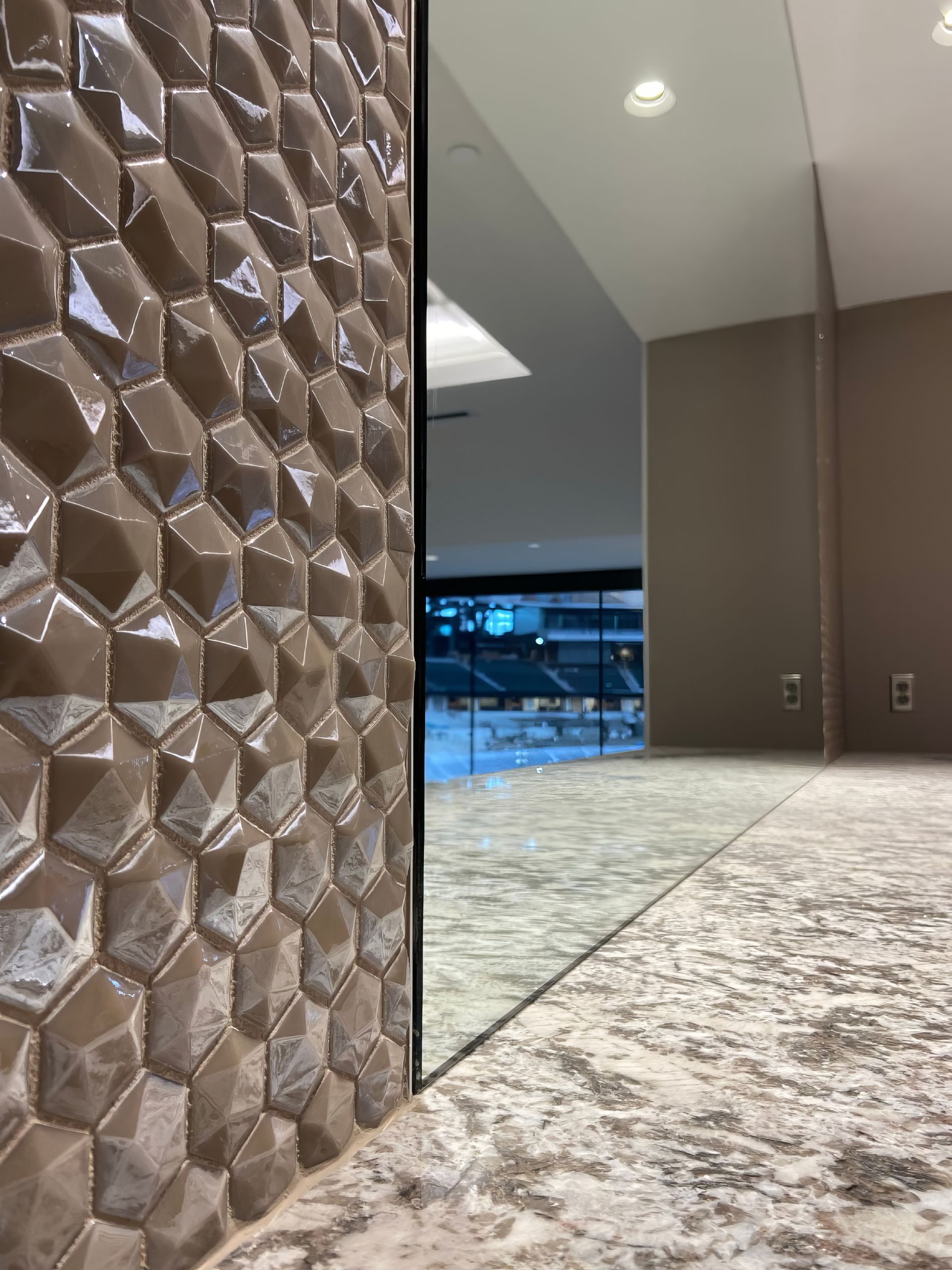 Textured wall beside a large mirror in a modern room with a patterned carpet and distant window view