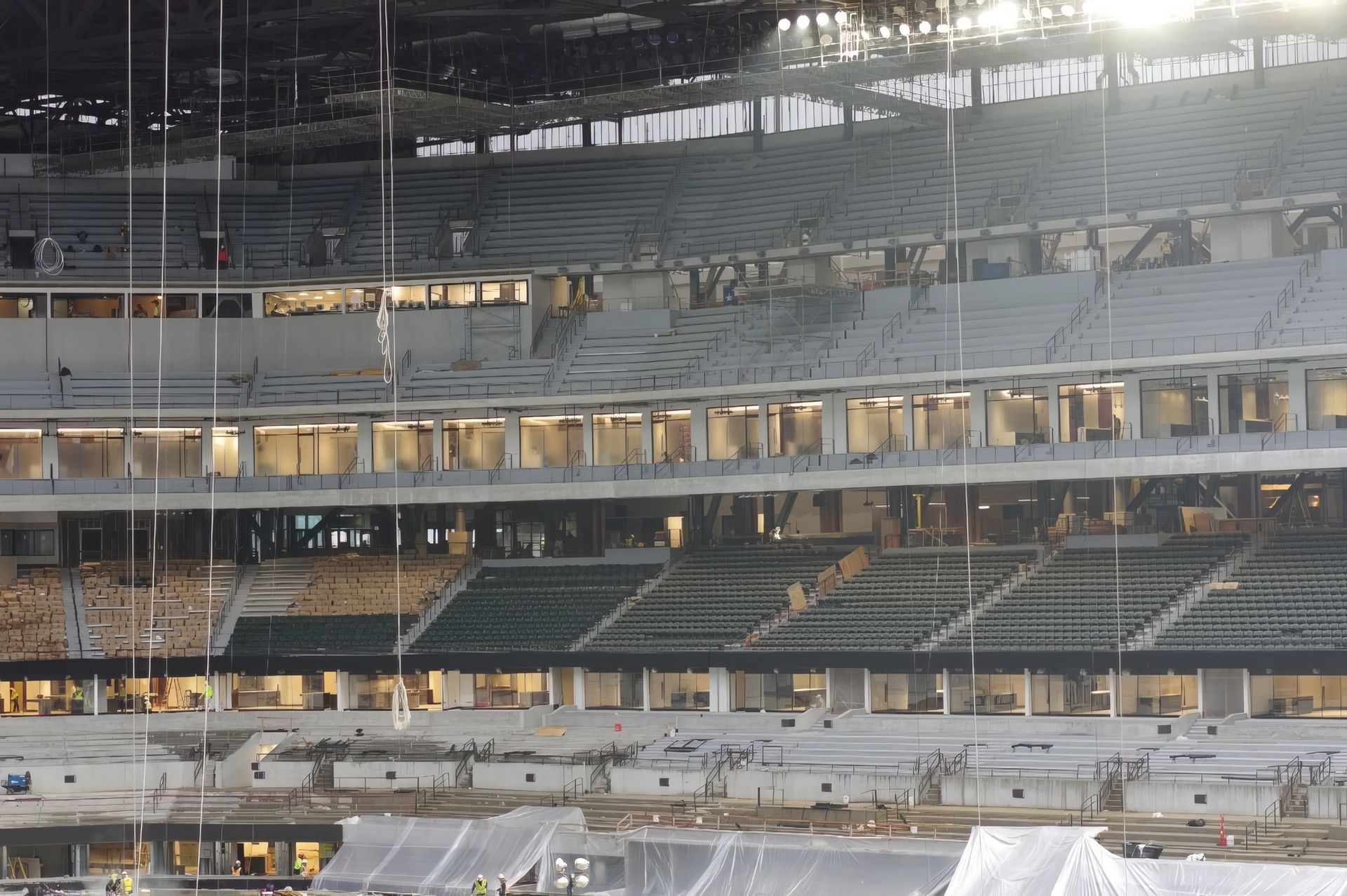 Interior of a large stadium under construction, with tiered seating and exposed beams under bright lights