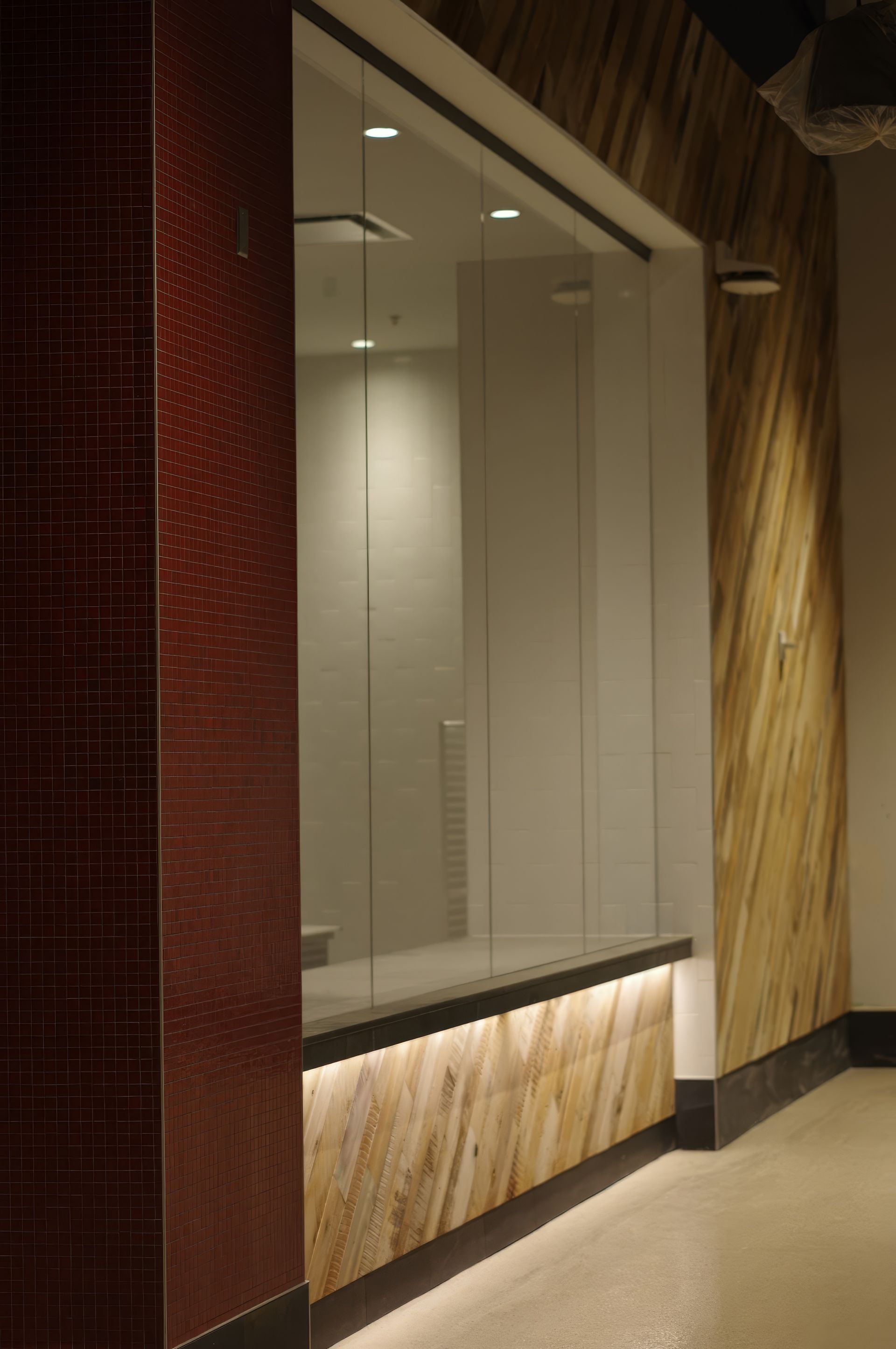 Empty storefront window with blinds, red tiled wall, and wood-paneled base in a hallway