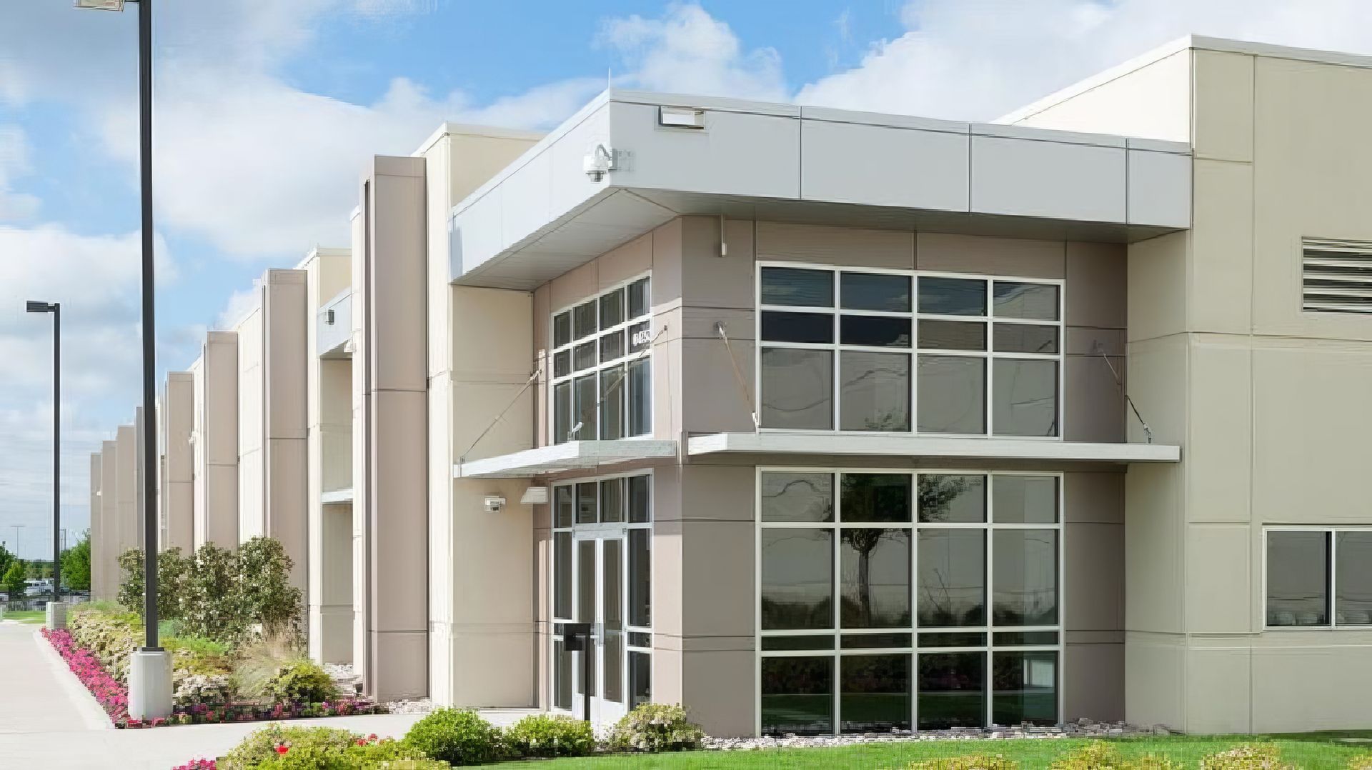 Modern commercial building exterior with large windows and beige siding under a partly cloudy sky