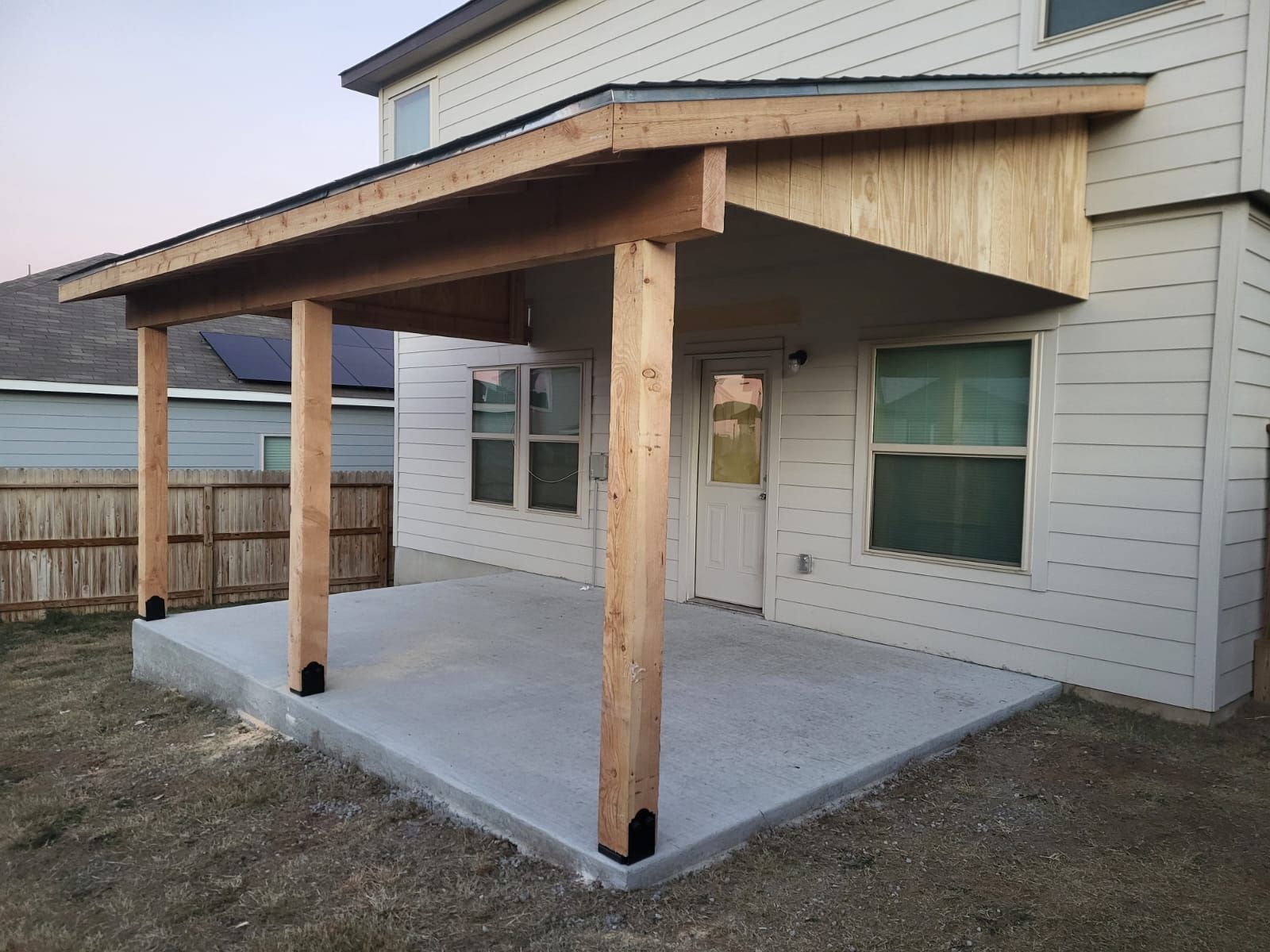 A patio with a wooden roof is in the backyard of a house.