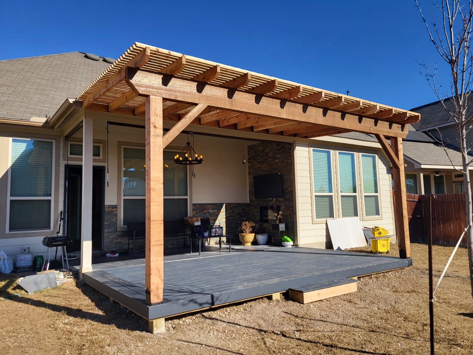 A wooden pergola is sitting on top of a deck in front of a house.