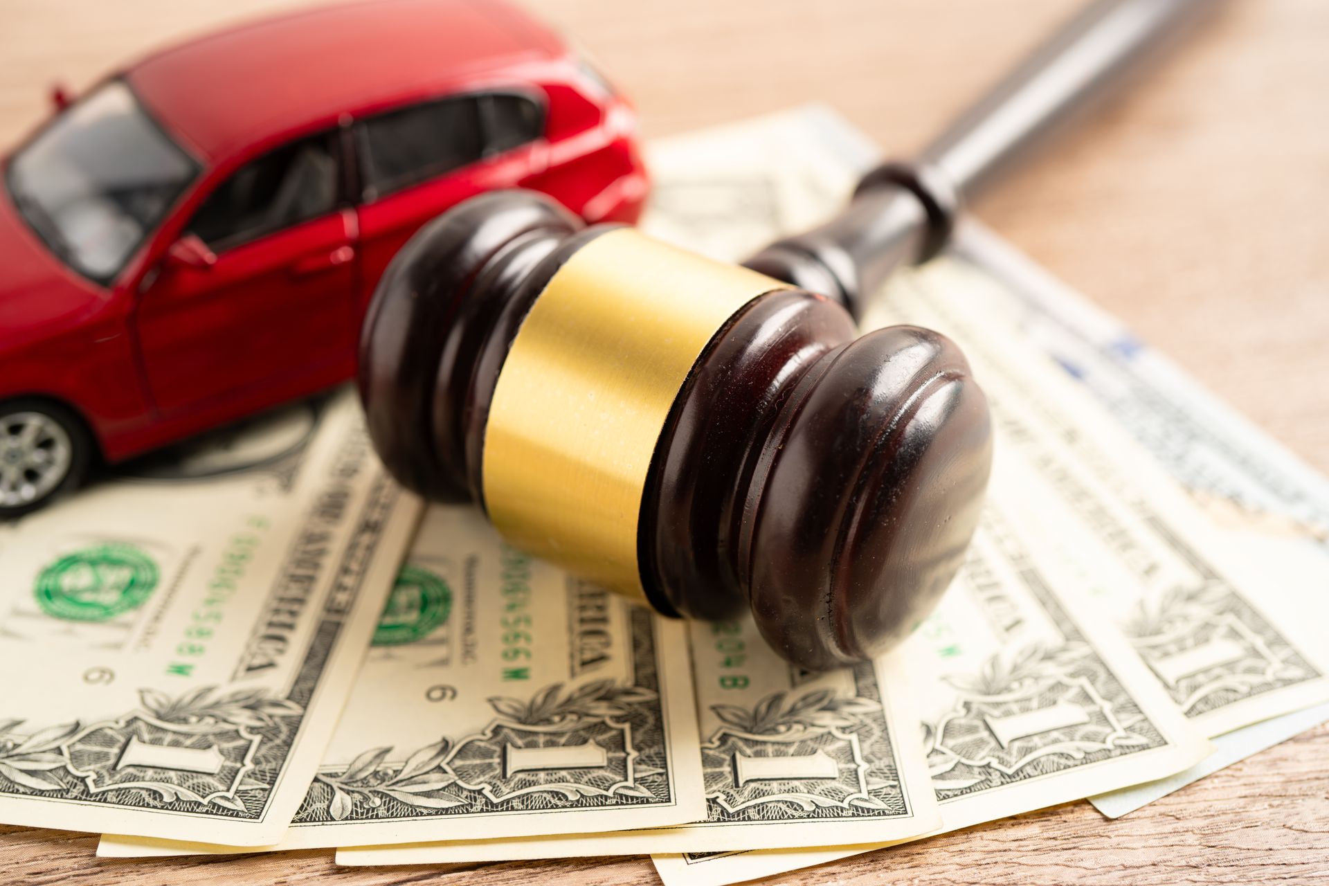 Toy red car, gavel, and dollar bills, representing car auction or legal proceedings.