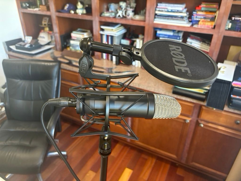 A microphone with a pop filter on a stand in front of a wooden bookshelf.
