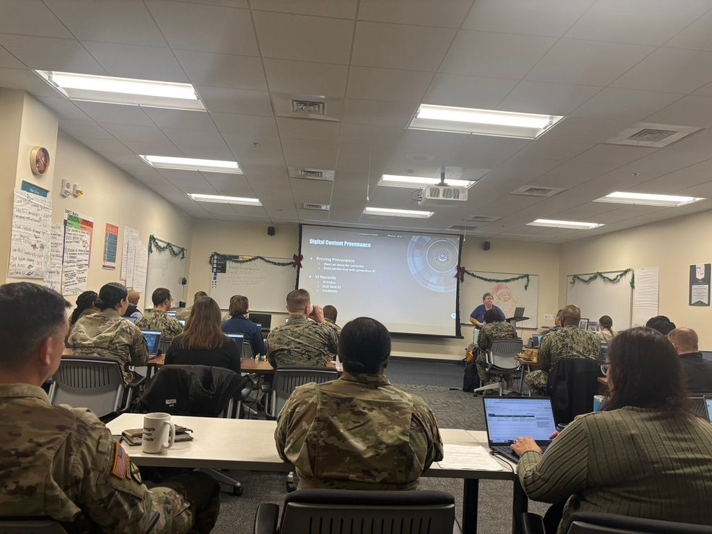 Classroom with people in military uniforms listening to a presentation on a projector screen.
