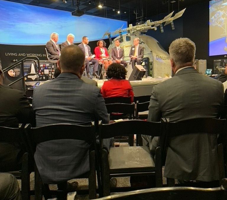 Panel of six people on stage, audience members in front.