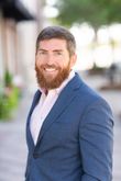 Smiling bearded man in a blue blazer outdoors with a blurred background