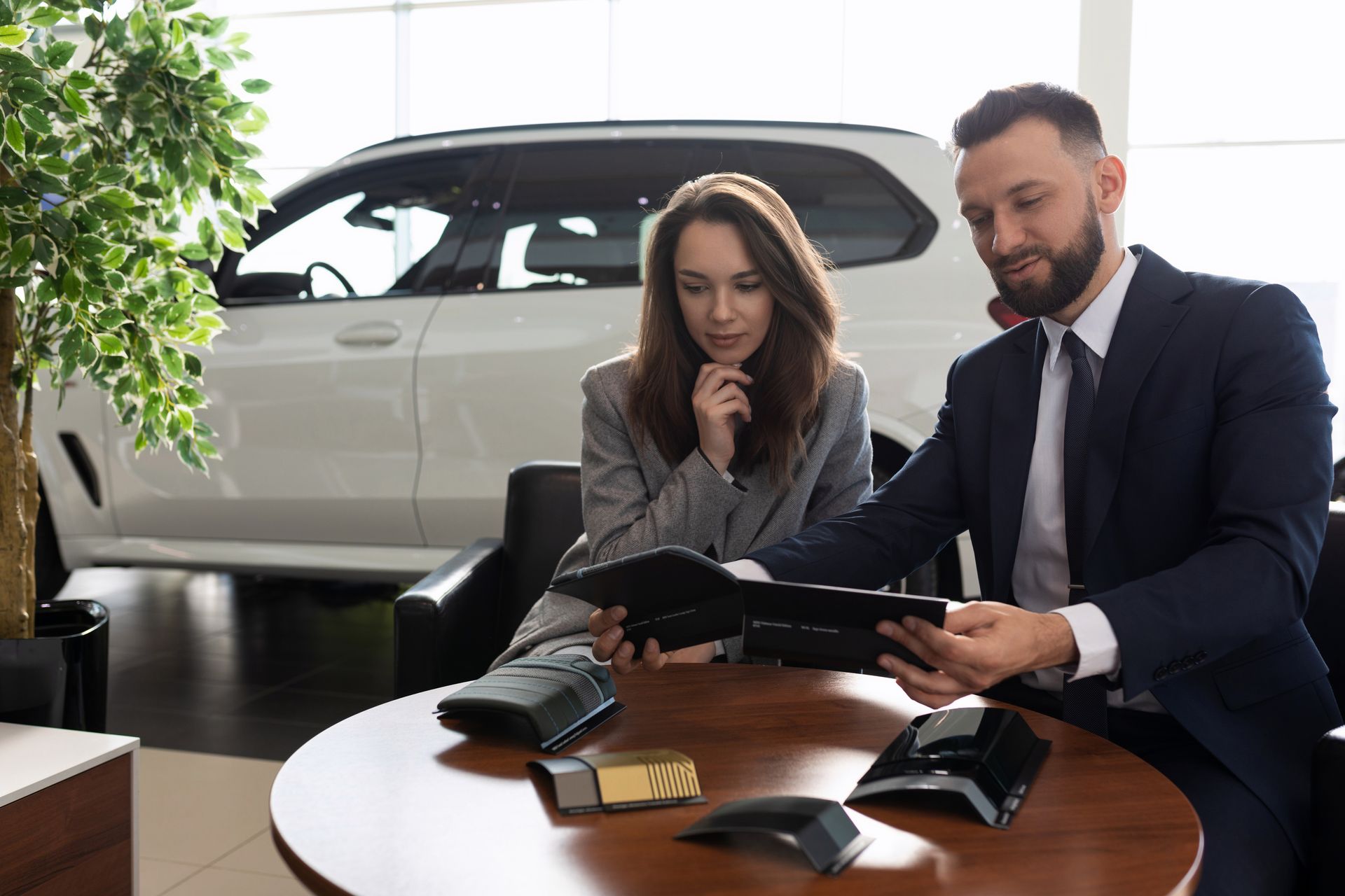 Two businesspeople reviewing a car brochure at a table in a bright showroom