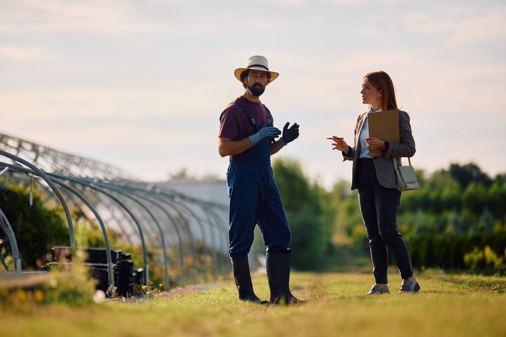 Two people talking beside a greenhouse in a sunny field