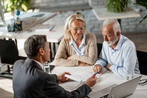 Three people in a meeting reviewing documents at a table with a laptop