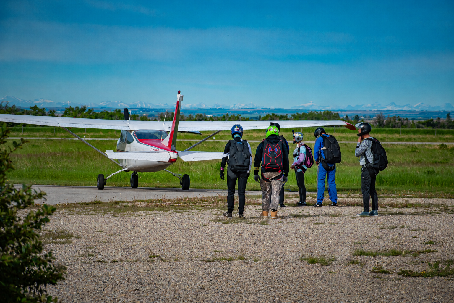 Five skydivers with parachutes beside a small red-and-white airplane on a airstrip.