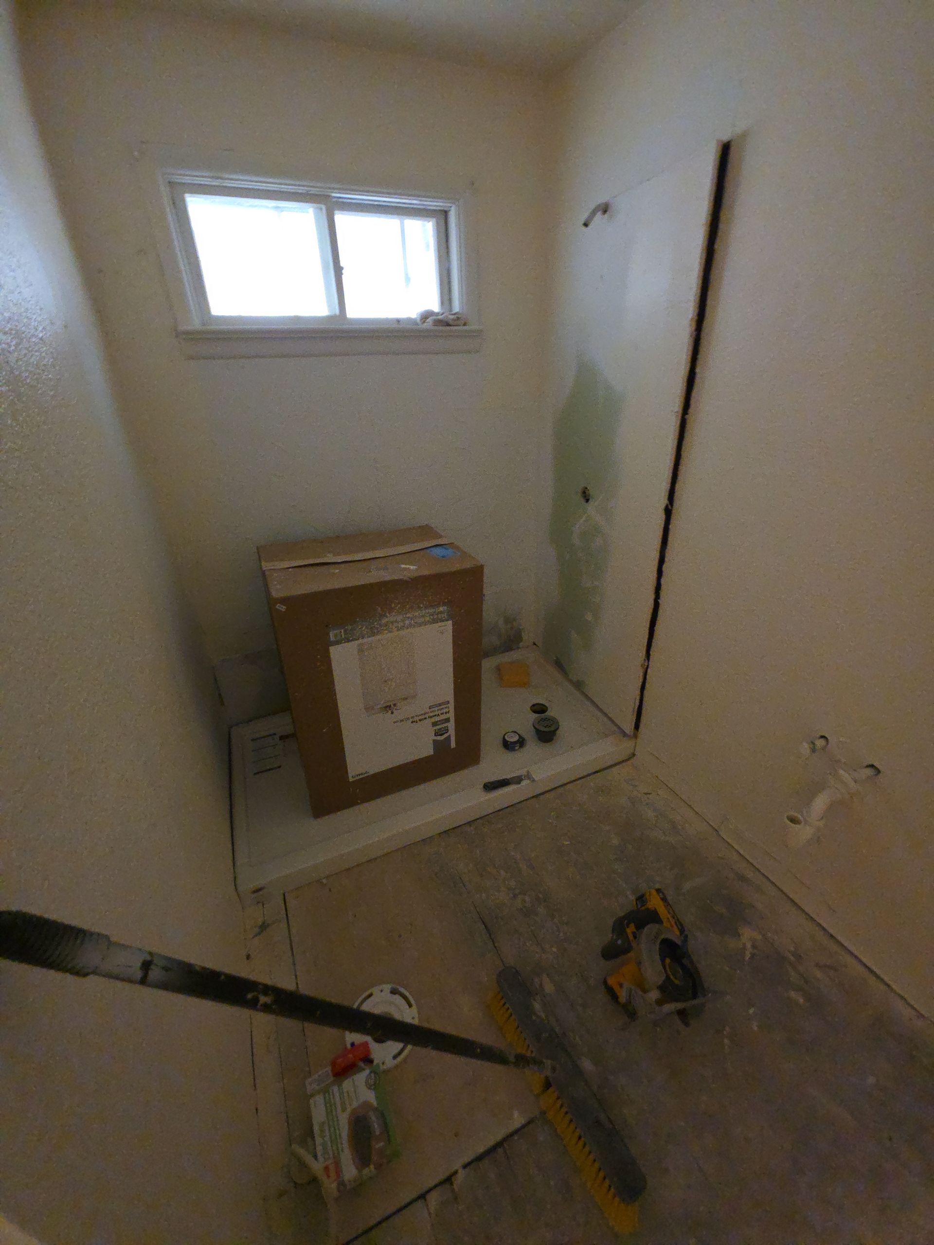 Small bathroom under renovation with a window, toilet box, tools, and debris on the floor.
