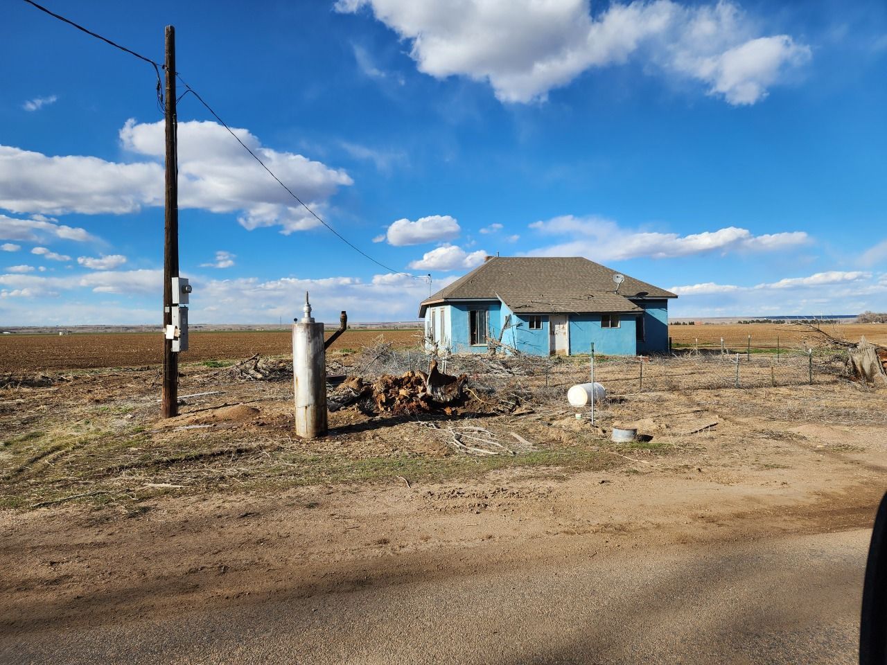 Small blue house in a dry rural landscape under a bright blue sky with clouds.