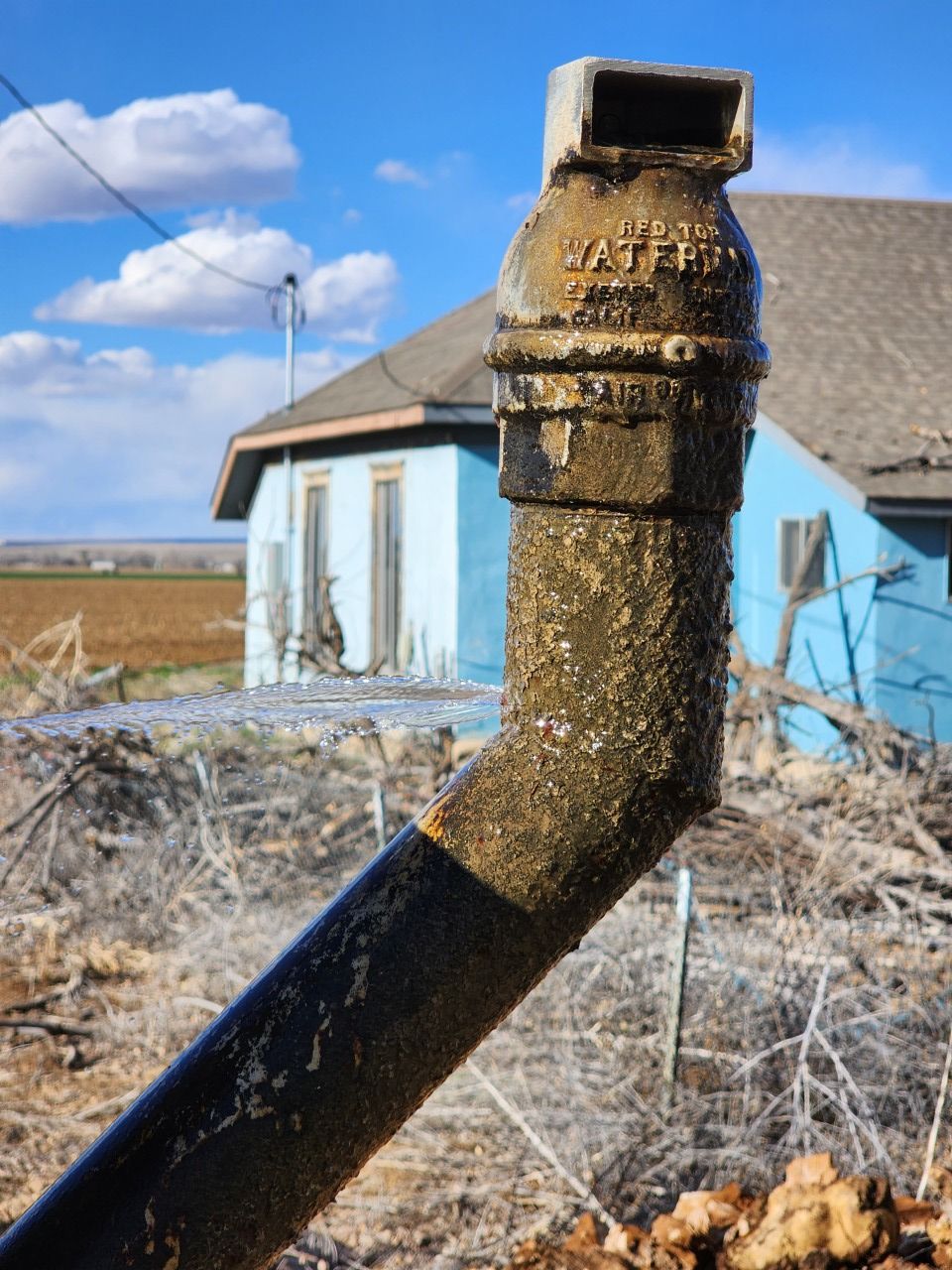 Icy black metal pipe beside a blue house in a frozen rural yard