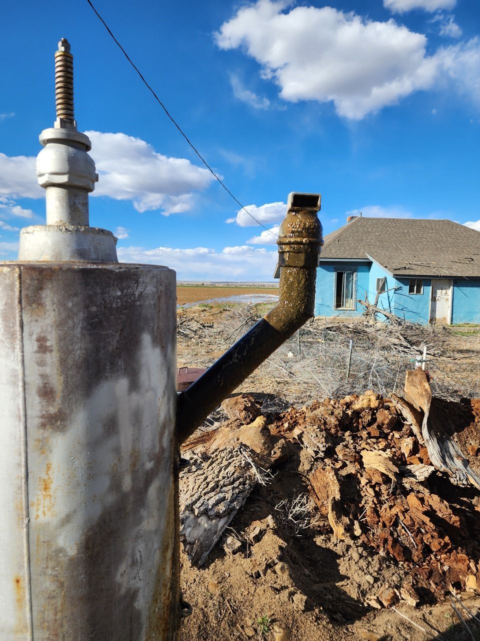 Damaged metal pipe in a muddy excavation beside a blue house under a bright sky