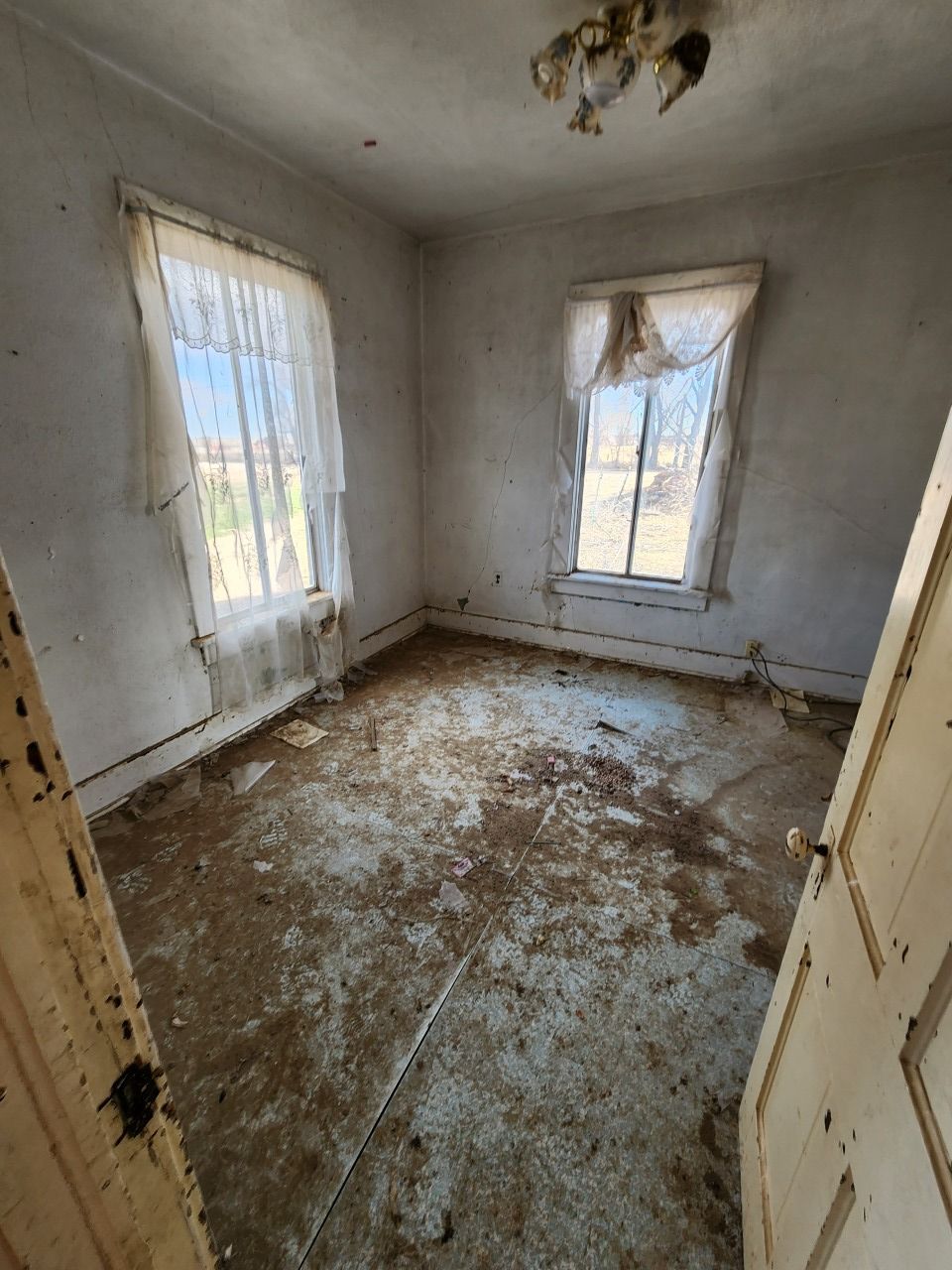 Abandoned small room with peeling floor, stained walls, and two windows with sheer curtains Abandoned small room with peeling floor, stained walls, and two windows with sheer curtains