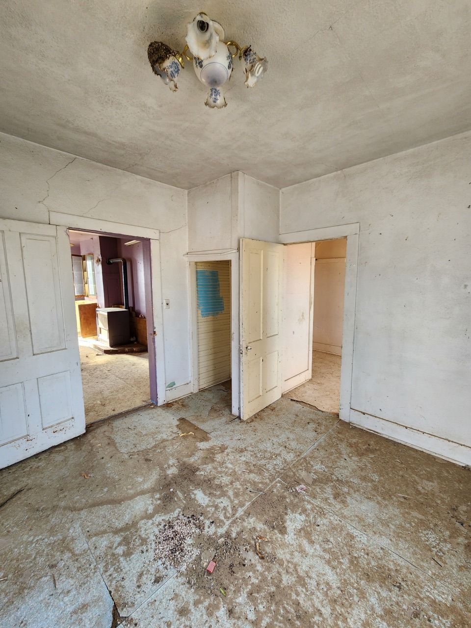 Empty, worn room with peeling white paint, open doorways, and a damaged ceiling light fixture