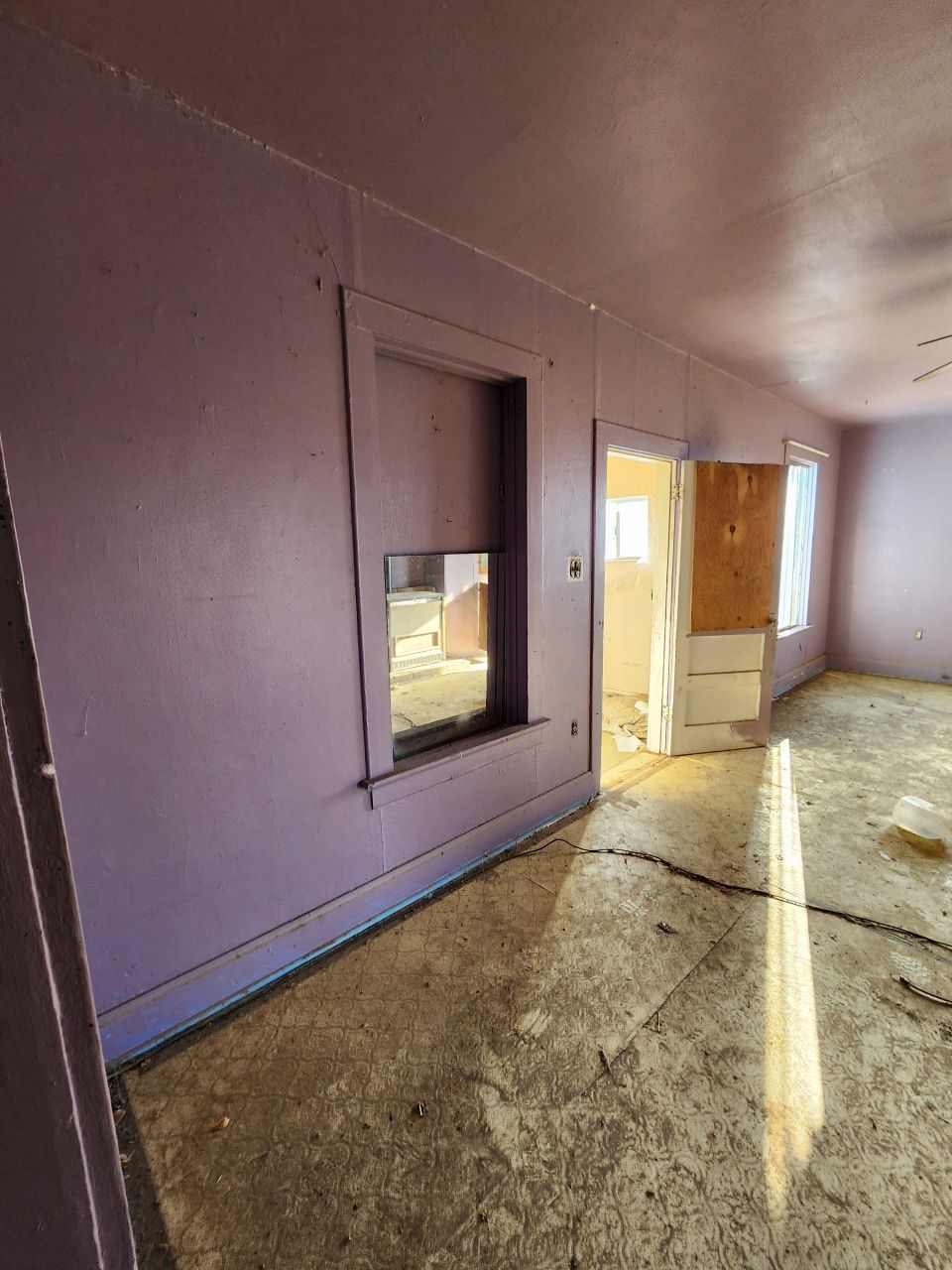 Empty room with lavender walls, a window, and sunlight streaming across a worn floor Empty room with lavender walls, a window, and sunlight streaming across a worn floor
