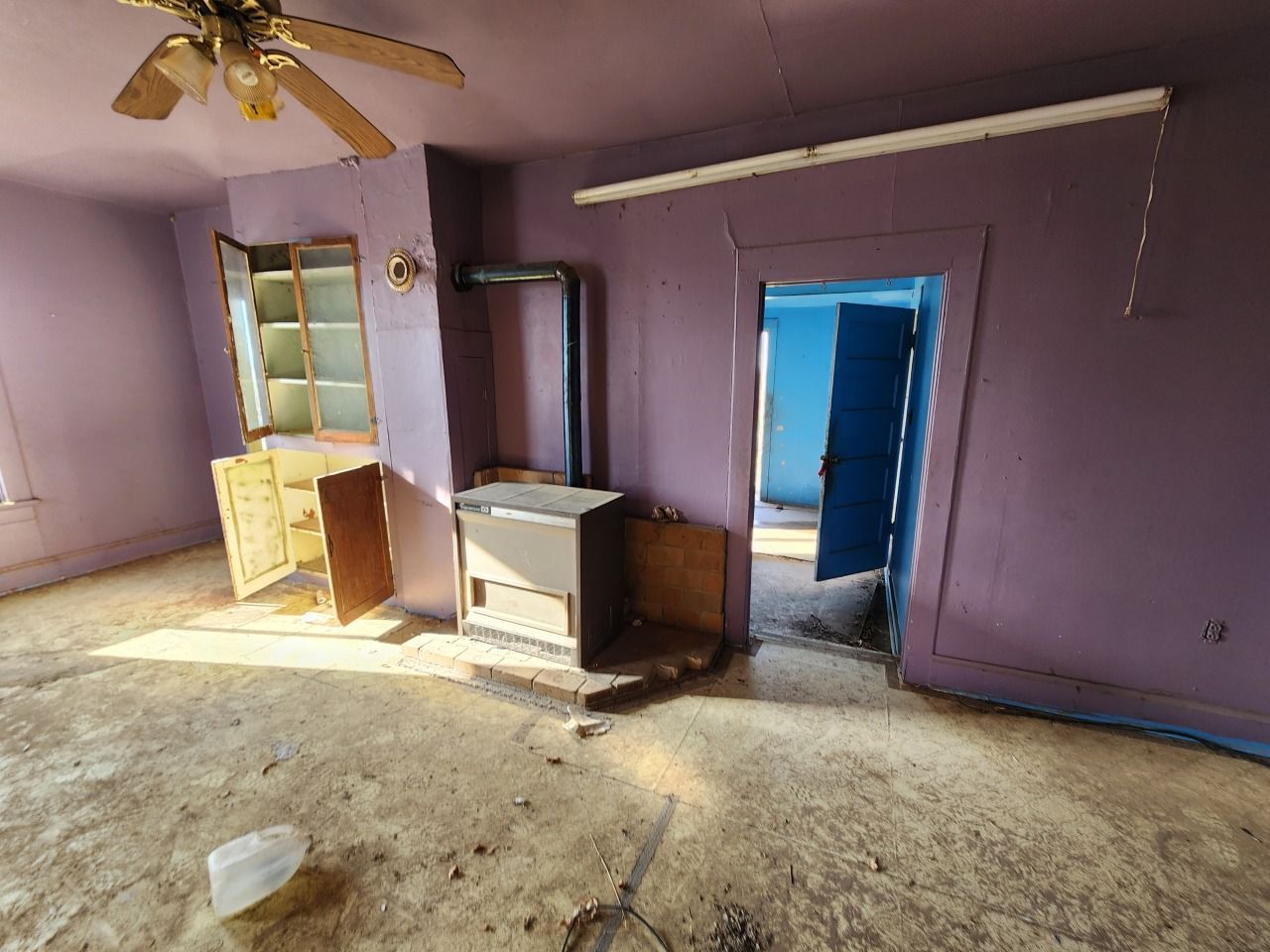 Empty purple room with ceiling fan, dresser, and open doorway to blue hallway.