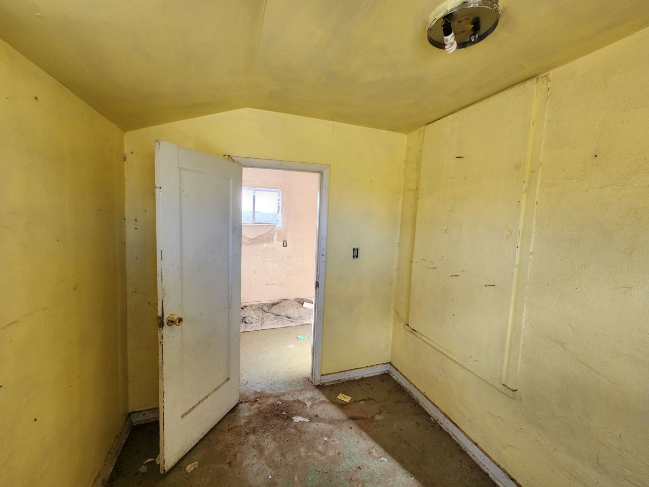 Small yellow room with open door, bare walls, and a damaged floor leading to another room Small yellow room with open door, bare walls, and a damaged floor leading to another room