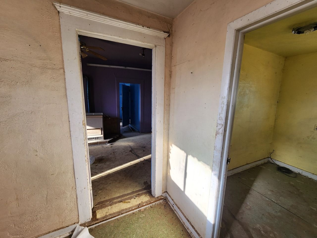Empty hallway with open doorways into dim rooms, beige walls, and sunlight on the floor
