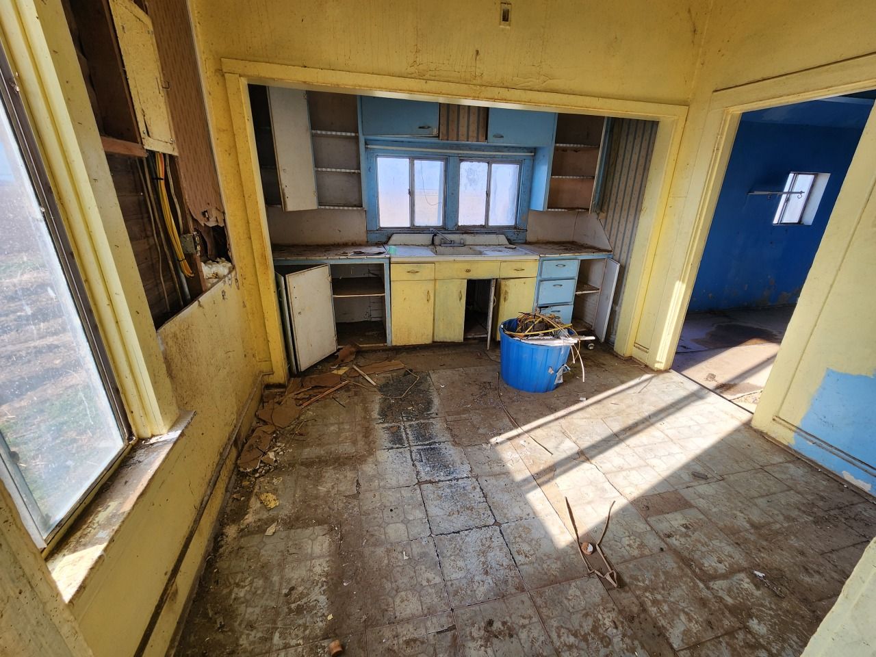 Abandoned kitchen with yellow walls, broken floor, and scattered debris, lit by sunlight through windows. Abandoned kitchen with yellow walls, broken floor, and scattered debris, lit by sunlight through windows.