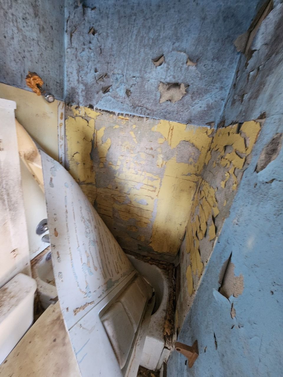Damaged blue and yellow wall with peeling paint and debris in a narrow stairwell