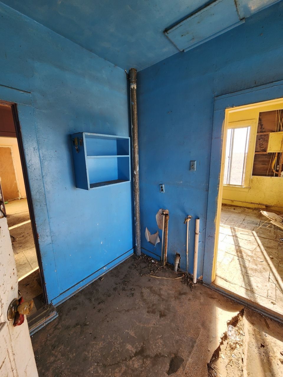 Blue room with bare floor, exposed pipes, and sunlight through a doorway into a yellow room. Blue room with bare floor, exposed pipes, and sunlight through a doorway into a yellow room.