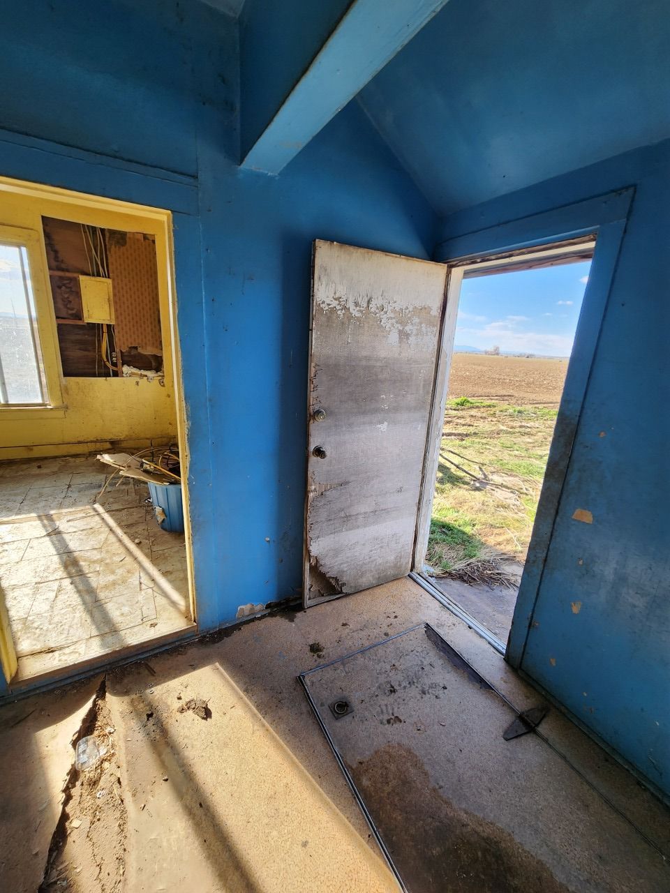 Blue empty room with open door and window, sunlight on dusty floor, view of bare ground outside Blue empty room with open door and window, sunlight on dusty floor, view of bare ground outside